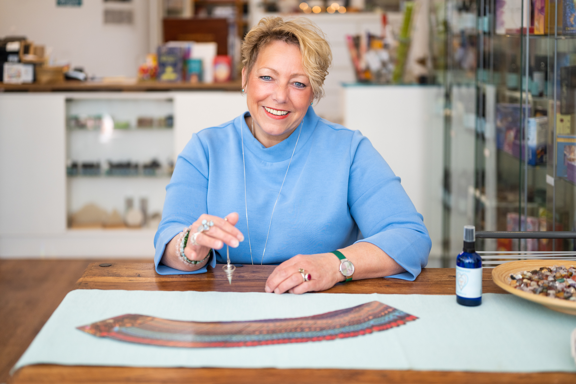 Hanneke Roebbers aan tafel in haar winkel Ohanna's World, tussen kristallen en kaarten